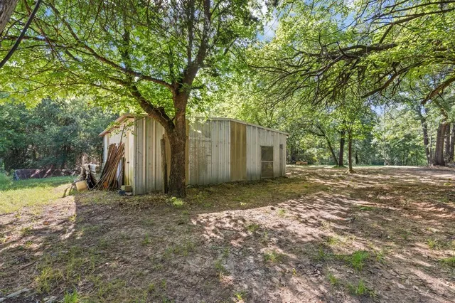 a view of a backyard with large trees and a small barn
