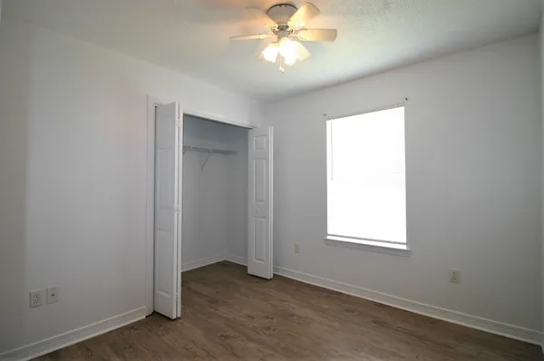 an empty room with wooden floor closet and windows