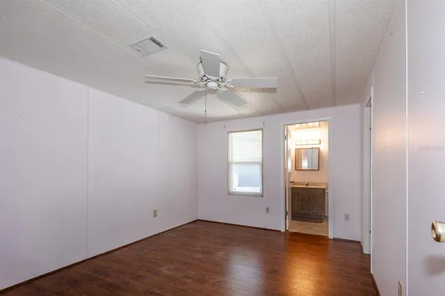 an empty room with wooden floor fan and windows
