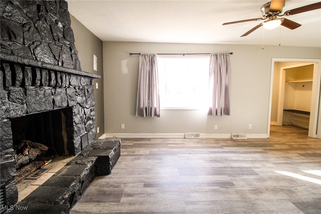 3267 South Leavitt Road Southwest Warren, OH 44481 - Photo 17 of 45 Unfurnished living room with light wood-style floors, a stone fireplace, and a ceiling fan