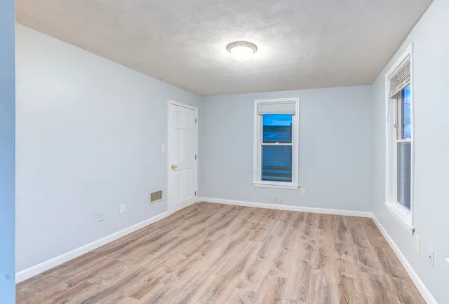 a view of an empty room with window and wooden floor