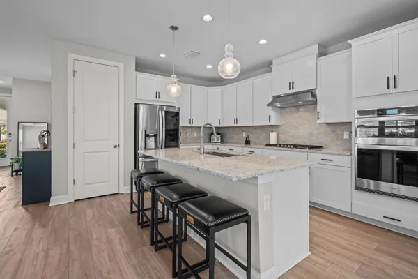 a kitchen with kitchen island granite countertop a sink a stove a refrigerator and white cabinets with wooden floor