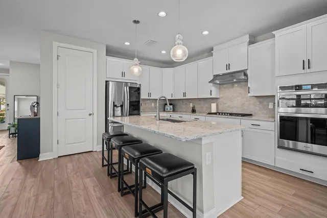 a kitchen with kitchen island granite countertop a sink a stove a refrigerator and white cabinets with wooden floor