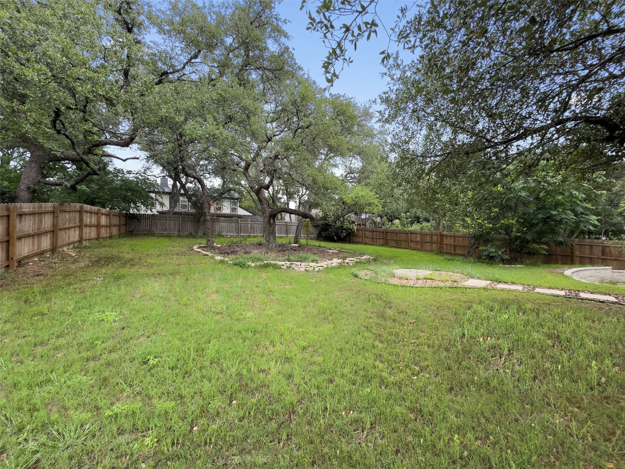 307 Hurst Creek Road Austin, TX 78734 - Photo 40 of 40 Spacious backyard featuring a wood privacy fence, mature trees, a central planting bed with stone edging, and a circular paved area