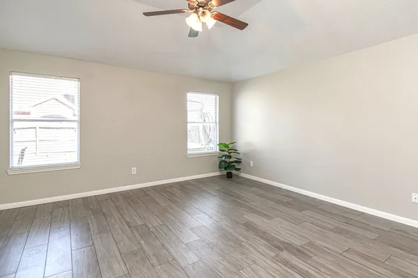 an empty room with wooden floor chandelier fan and windows