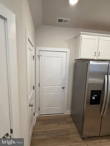 a view of a refrigerator in kitchen and an empty room with wooden floor