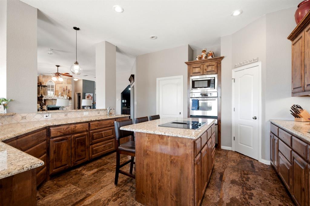600 Aspen Street Pilot Point, TX 76258 - Photo 17 of 39 Kitchen featuring an island with a built-in cooktop, light-toned countertops, rich wood cabinetry, stainless steel built-in appliances, and natural-toned flooring