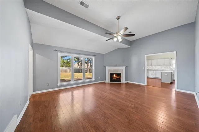 an empty room with wooden floor fireplace and windows
