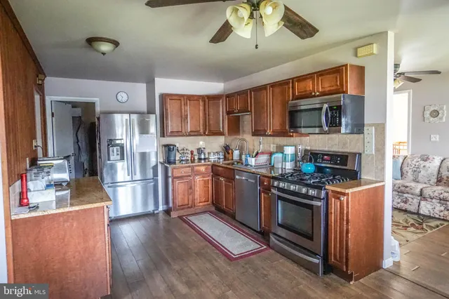 a kitchen with stainless steel appliances granite countertop a stove top oven a sink dishwasher a refrigerator and a dining table with wooden floor