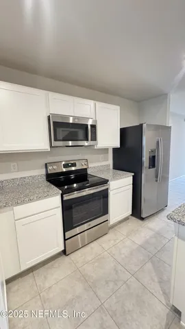 a kitchen with granite countertop a stove and a refrigerator with white cabinets