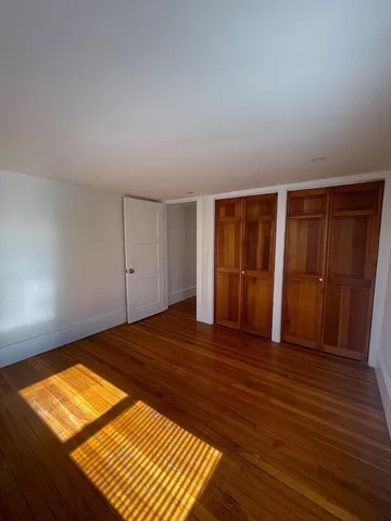 a view of an empty room with wooden floor and closet