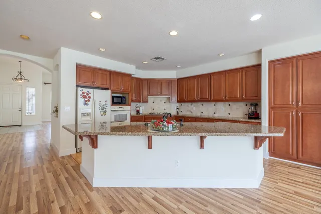 a kitchen with stainless steel appliances granite countertop a refrigerator a stove top oven a sink dishwasher and wooden cabinets with wooden floor