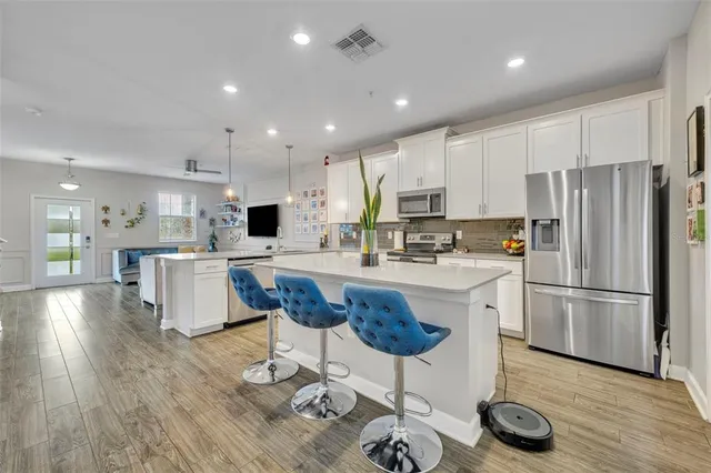 a kitchen with stainless steel appliances kitchen island granite countertop a refrigerator a stove a sink cabinets and a dining table with wooden floor