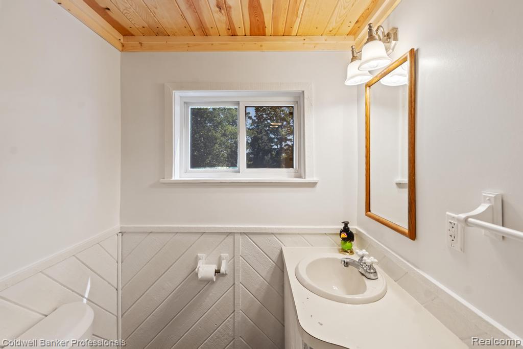 6389 Postlewait Road Mancelona, MI 49659 - Photo 37 of 50 Wood-paneled ceiling, white wood-finish wainscoting, white window, vanity with integrated sink, and wall-mounted light fixture