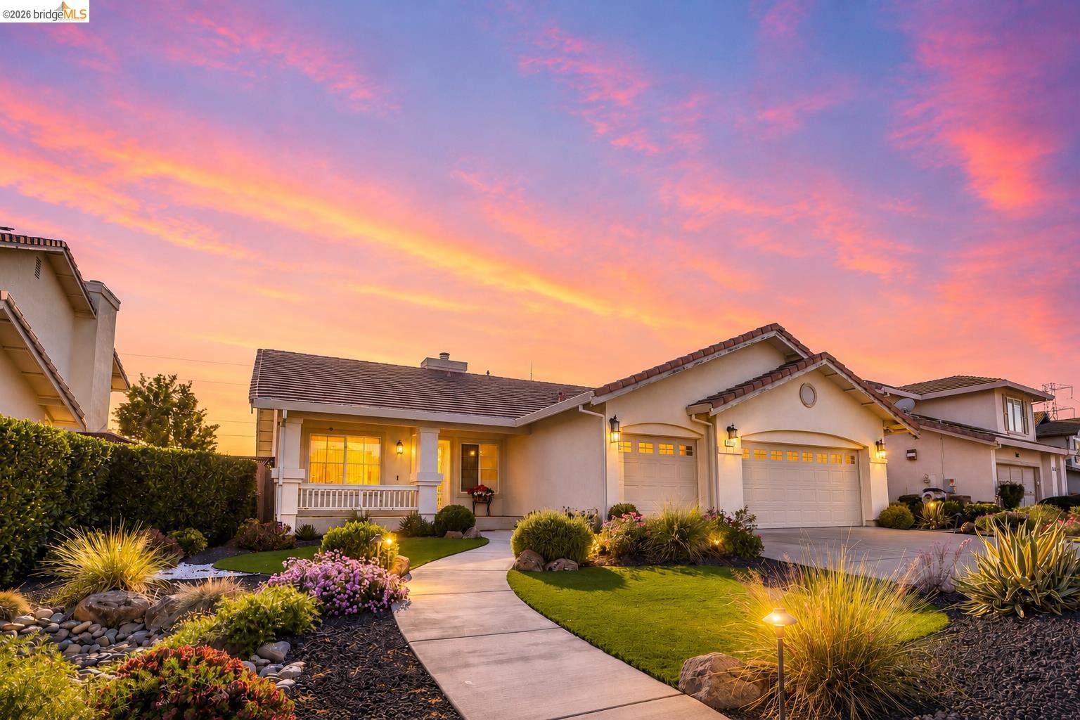 Stucco exterior residence with a multi-car garage, front porch featuring white columns and railing, and a winding concrete pathway