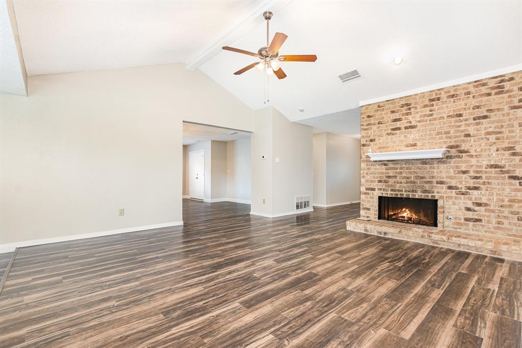 229 South Heartz Road Coppell, TX 75019 - Photo 2 of 18 Unfurnished living room with beam ceiling, wood finished floors, ceiling fan, a fireplace, and high vaulted ceiling
