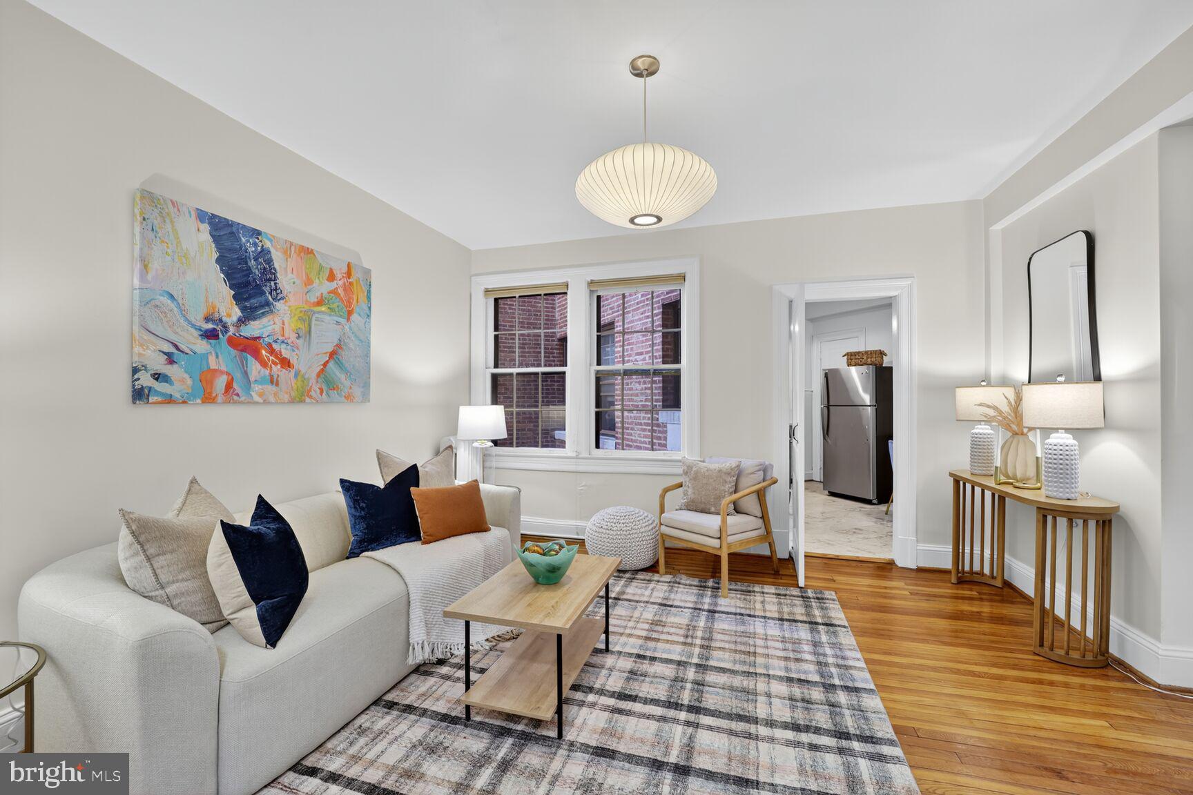 a living room with furniture two large window and wooden floor