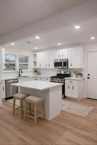a kitchen with stainless steel appliances kitchen island granite countertop a stove a sink a refrigerator and white cabinets with wooden floor