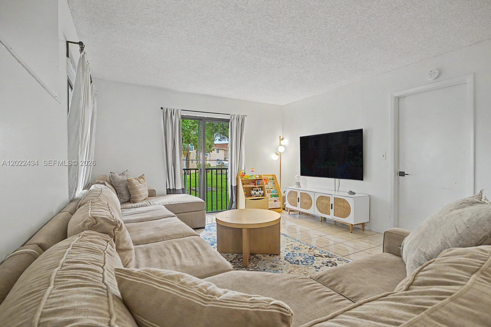 13045 Southwest 68th Street, Unit 111 Miami, FL 33183 - Photo 4 of 15 a living room with a couch a flat screen tv and a window