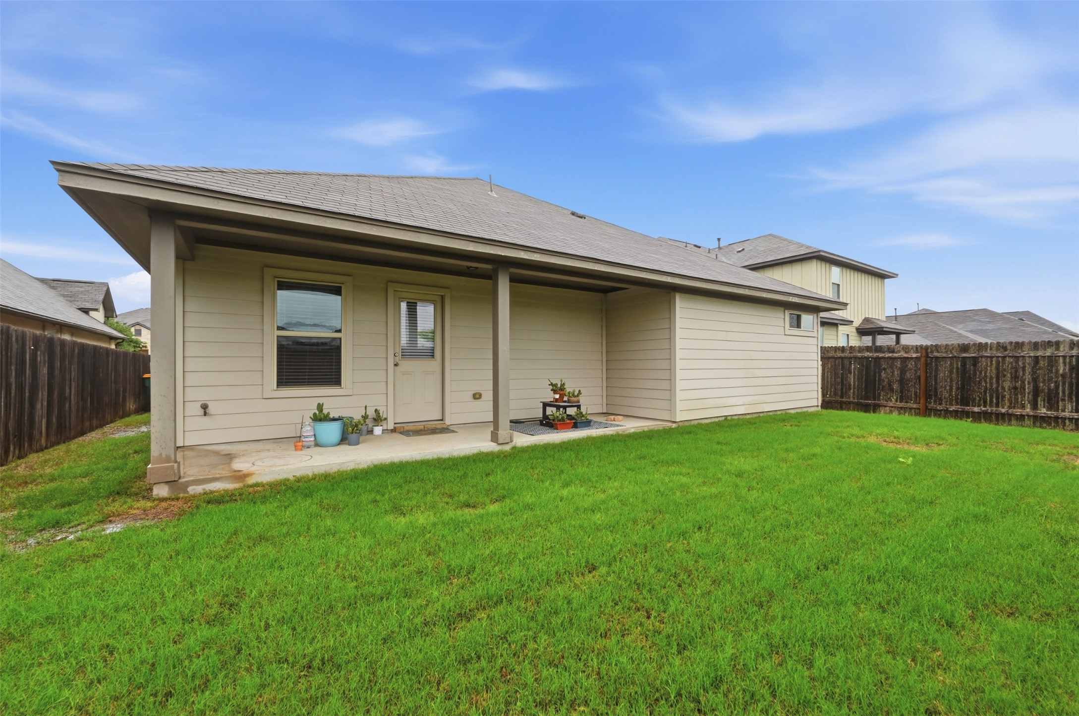 13116 Alans Way Manchaca, TX 78652 - Photo 25 of 25 Expansive green lawn with a covered patio, featuring privacy fencing, horizontal siding, and a gabled roofline