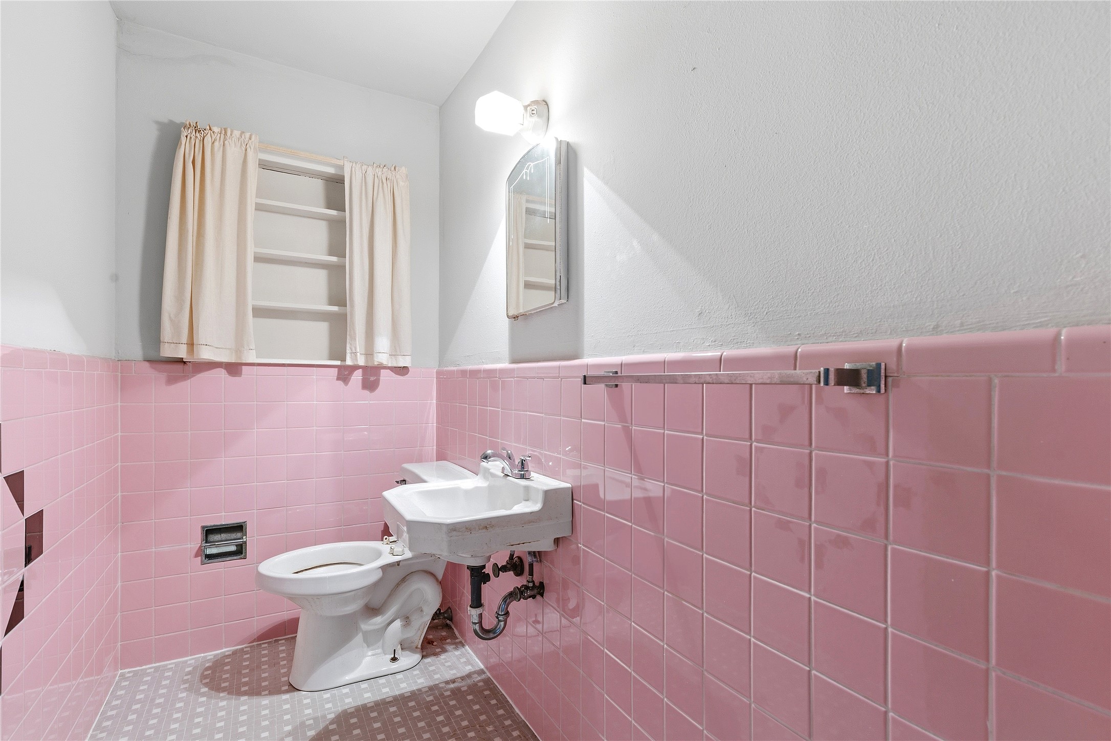 4900 Duval Street Austin, TX 78751 - Photo 19 of 25 Vintage half bath featuring original 1950s pink tile, original wall-mounted sink, mirror, light fixture, and classic period details. A charming example of the home’s preserved mid-century character and restoration potential.
