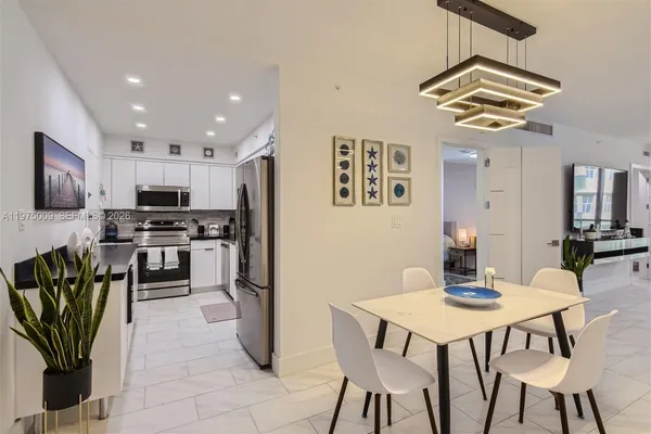 a kitchen with stainless steel appliances kitchen island granite countertop a dining table chairs and a refrigerator