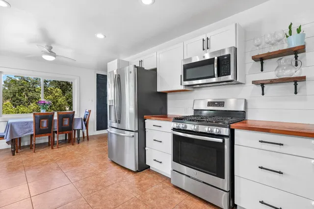 a kitchen with stainless steel appliances granite countertop a stove top oven a sink dishwasher a refrigerator and a dining table with wooden floor