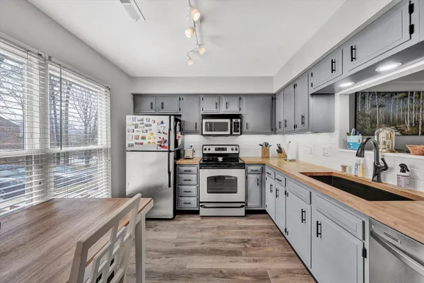 a kitchen with stainless steel appliances granite countertop a stove top oven a sink dishwasher a refrigerator and a cabinets with wooden floor