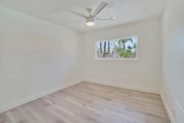 an empty room with wooden floor and ceiling fan