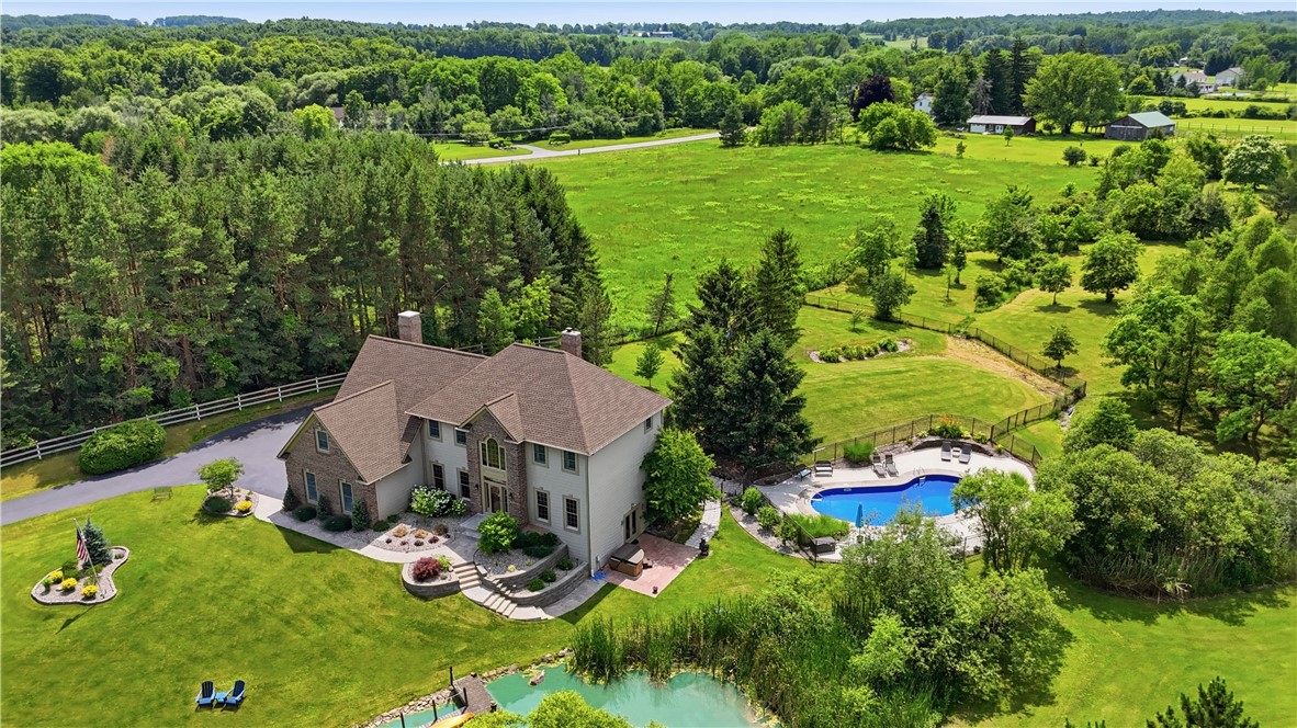 2057 Stirnie Road Victor, NY 14564 - Photo 1 of 48 Stunning aerial overview highlights the designed layout of the main residence and its surrounding outdoor amenities. Nestled on 5.10 acres of pristine country grounds, the property seamlessly connects the main living spaces to the in-ground pool, the lower-level walk-out patio, and the scenic edge of the private pond.