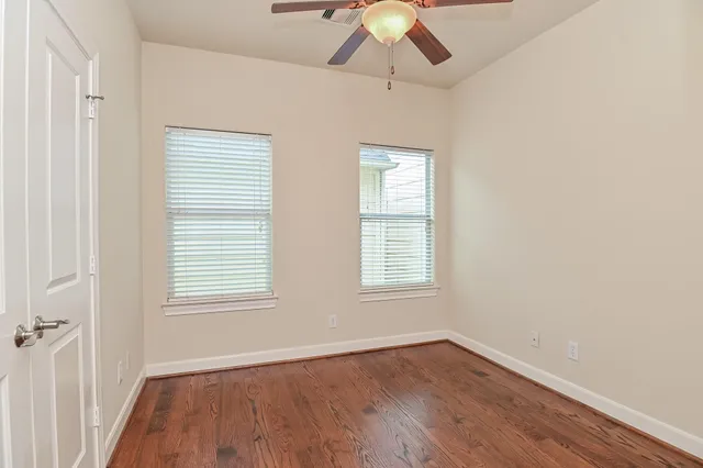 an empty room with wooden floor fan and windows