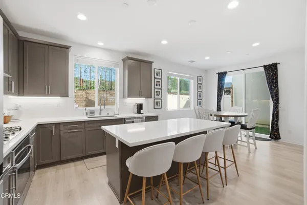 a dining hall with stainless steel appliances granite countertop a sink a stove a dining table and chairs with wooden floor