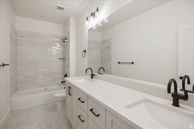 7189 South Sage Road, Unit 214 West Jordan, UT 84081 - Photo 19 of 29 Bathroom featuring a dual vanity with light cabinetry and integrated sinks, matte black fixtures, a white bathtub with subway tile surround, and a full-width mirror
