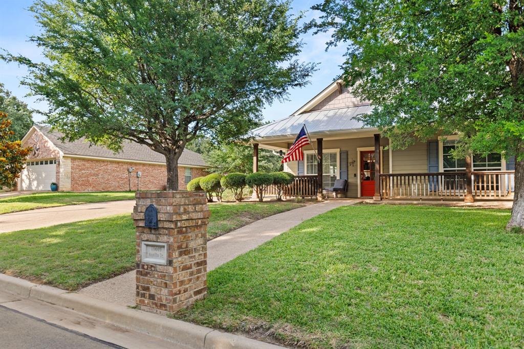 10609 Aquilla Trail Waco, TX 76708 - Photo 4 of 30 Charming cottage-style home featuring a covered front porch with a wood railing, light blue shutters, a red entry door, and a metal roof
