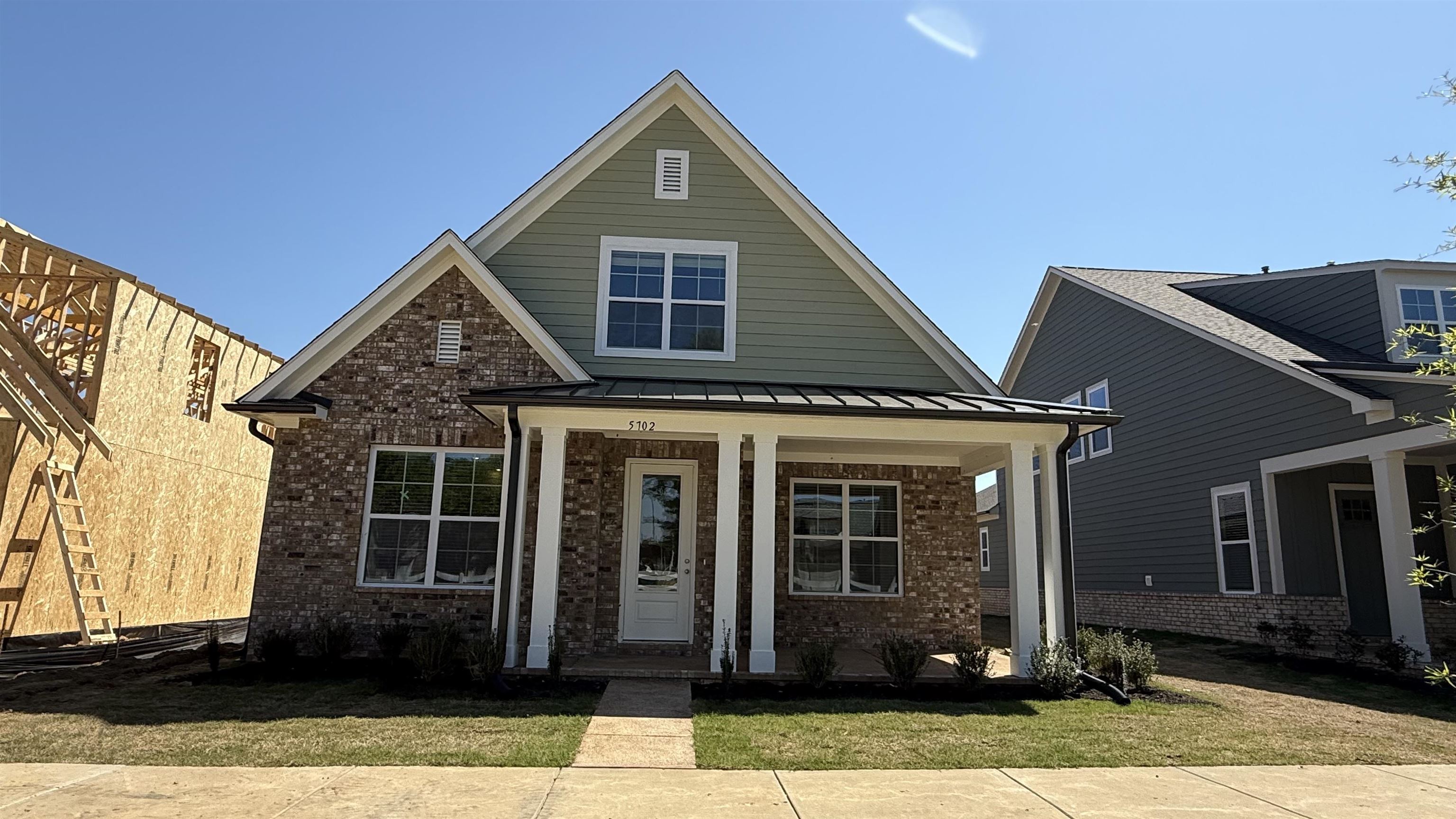 View of front facade with covered porch, a standing seam roof, brick siding, and a front lawn