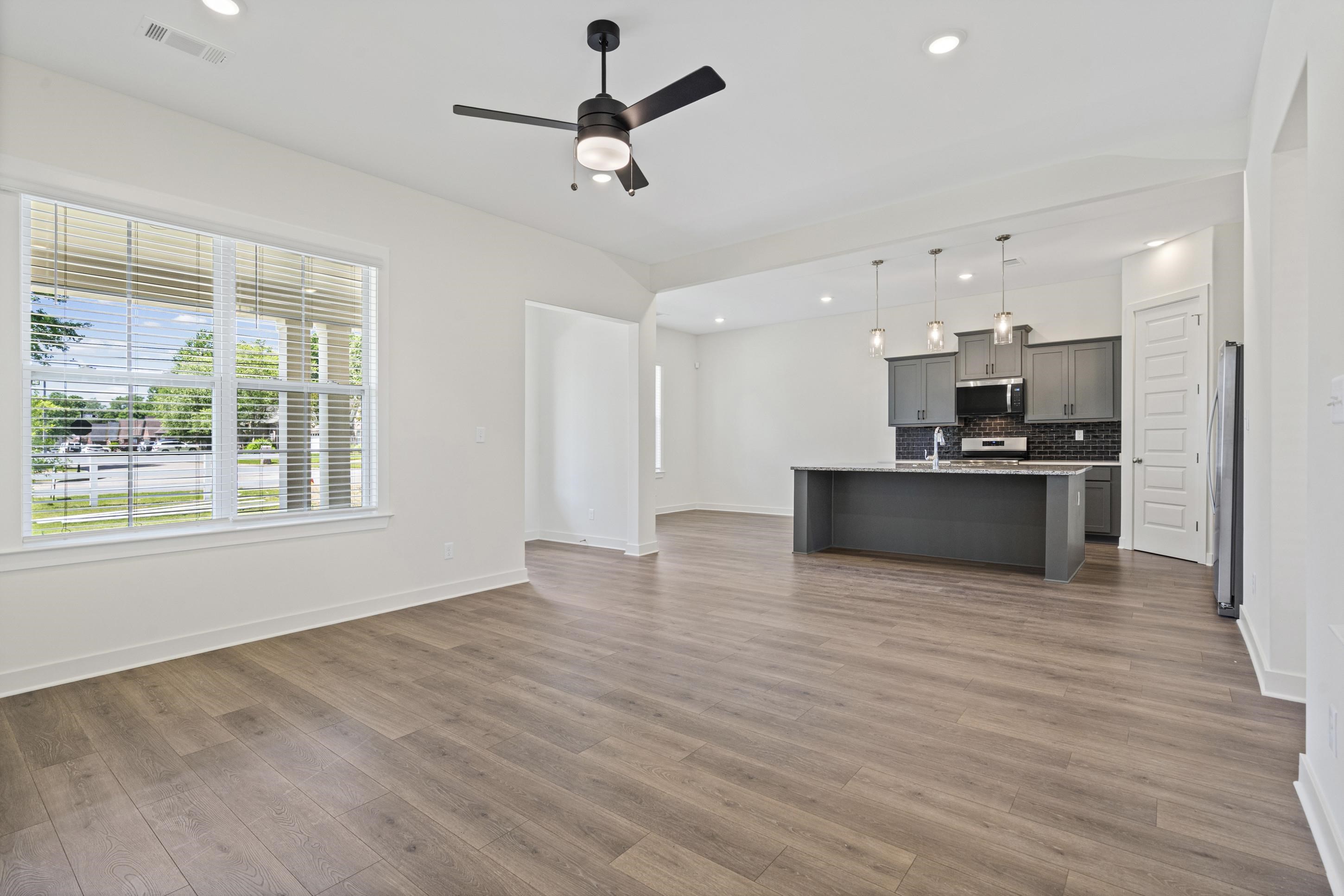 5702 Gerber Road Arlington, TN 38002 - Photo 6 of 27 Open-concept living space with wood-finish flooring, a large window with horizontal blinds, and a ceiling fan with integrated lighting
