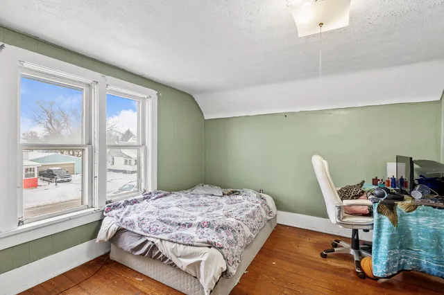 a bedroom with a bed wooden floor and a large window