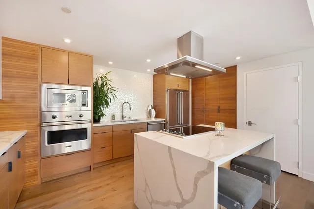 a room with stainless steel appliances a stove a refrigerator a kitchen island a stove and a couch