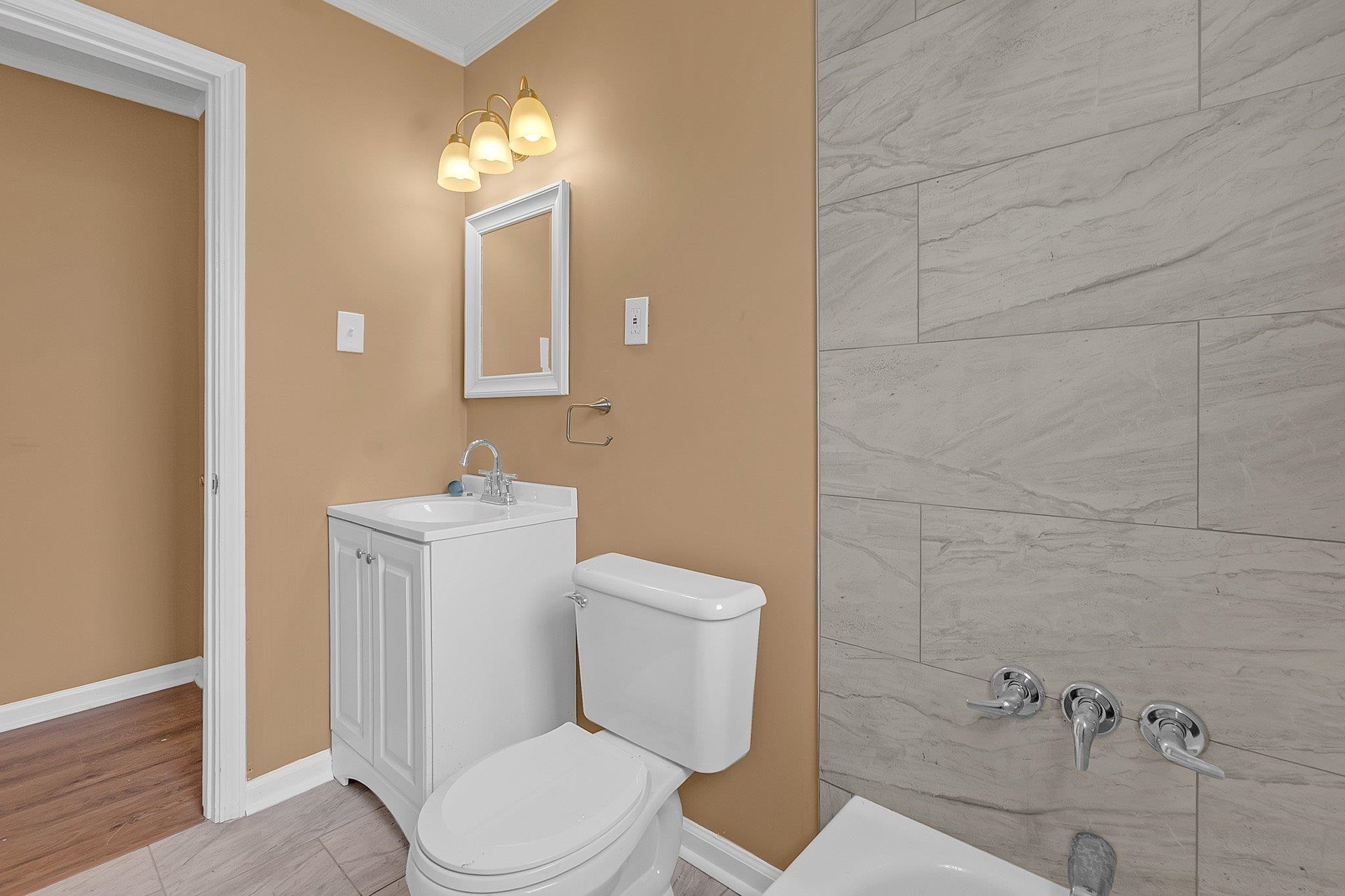 3186 Alta Road Memphis, TN 38109 - Photo 9 of 14 Bathroom featuring large format wall tiling, a white vanity with integrated sink, a white toilet, and a three-bulb wall sconce