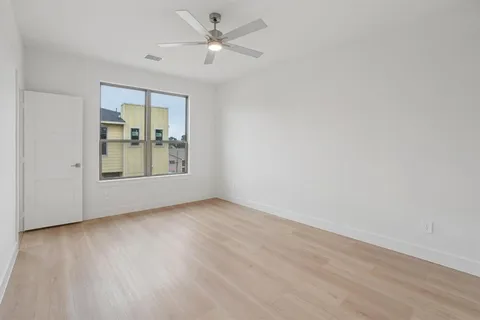 an empty room with wooden floor chandelier fan and windows