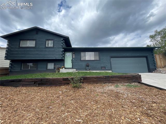View of front of home with log exterior, concrete driveway, and an attached garage