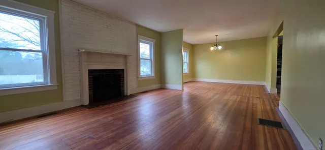 an empty room with wooden floor fireplace and windows