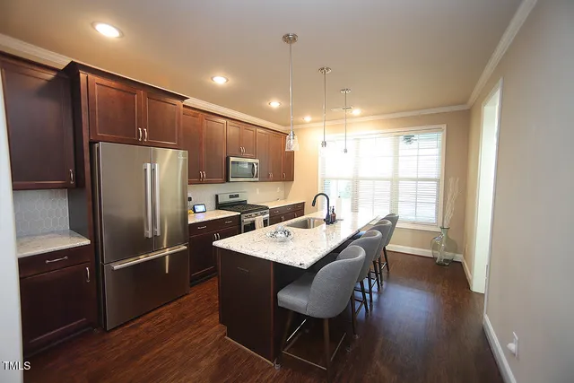 a kitchen with stainless steel appliances granite countertop a refrigerator a sink a stove a dining table and chairs