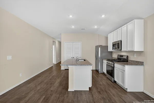 a kitchen with stainless steel appliances granite countertop a stove top oven a sink dishwasher and a refrigerator with wooden floor