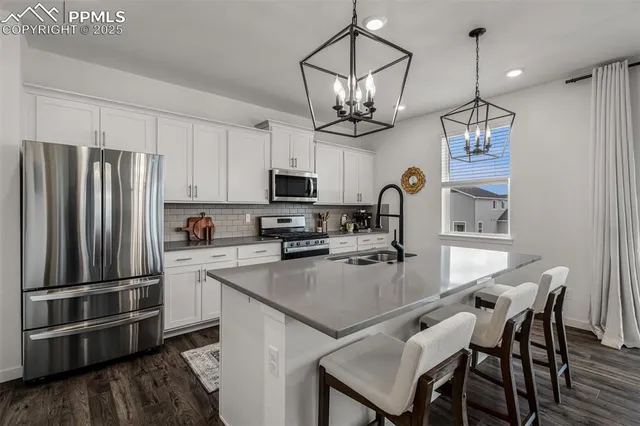 a kitchen with stainless steel appliances granite countertop a sink a stove a refrigerator cabinets a dining table and chairs