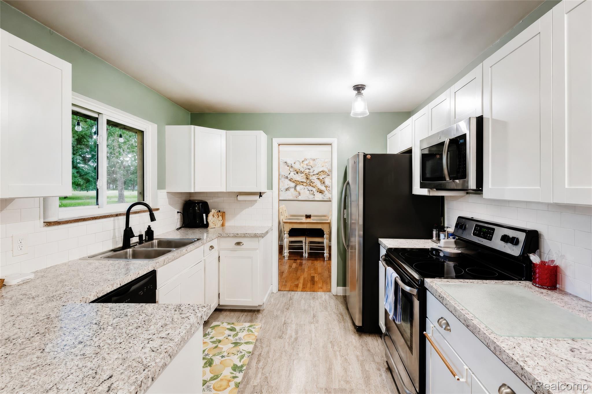 4499 South Linden Road Flint, MI 48507 - Photo 18 of 36 Well-appointed kitchen featuring white cabinetry, light-toned countertops, a white subway tile backsplash, stainless steel appliances, and wood-finish flooring