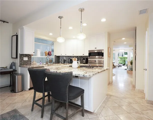 a kitchen with stainless steel appliances granite countertop a sink a stove a refrigerator and chairs