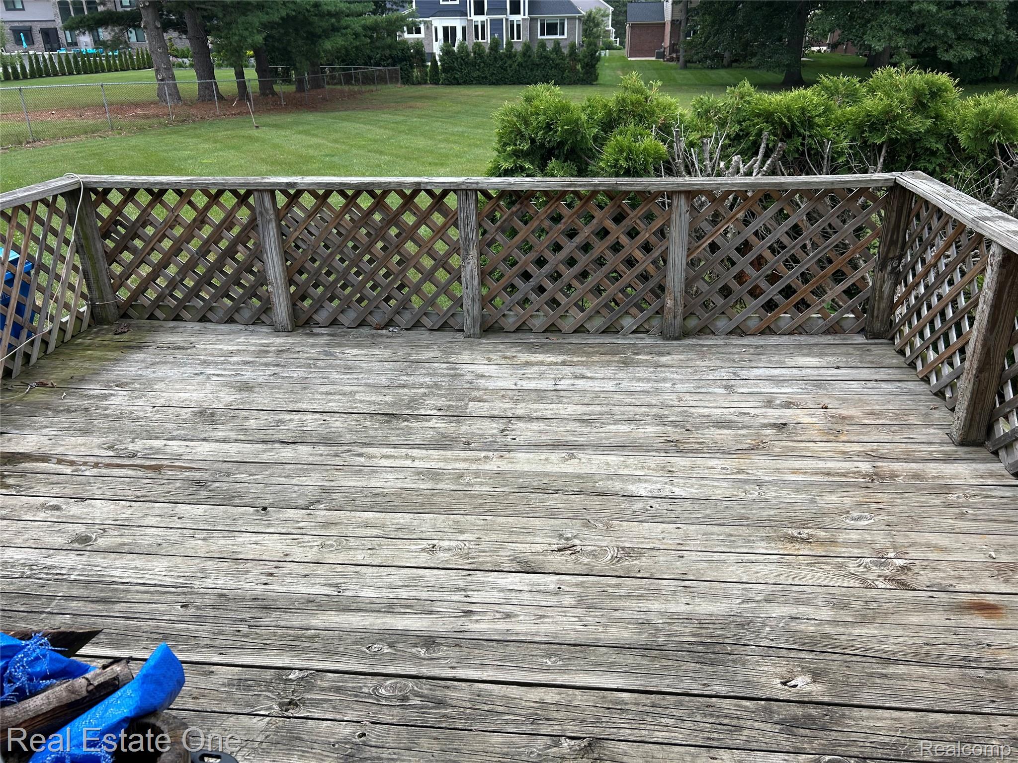 2659 Benstein Road Commerce Township, MI 48382 - Photo 23 of 26 Outdoor wood deck with lattice railing, overlooking a green lawn with mature trees and distant residential structures
