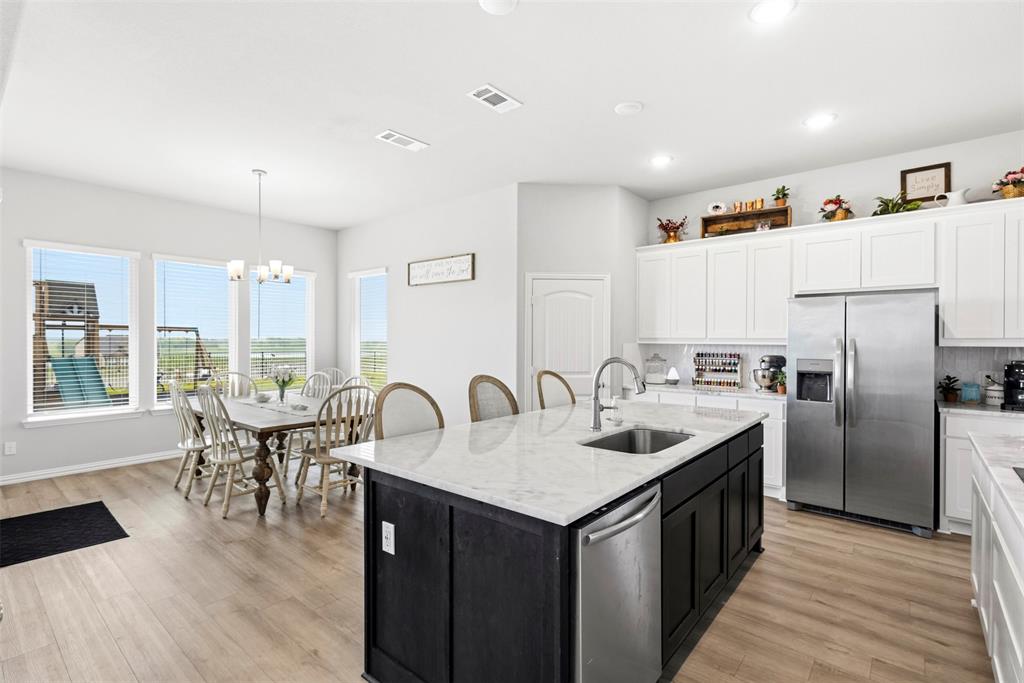 107 Yampa Court Rhome, TX 76078 - Photo 11 of 30 Open-concept kitchen featuring a large central island with sink, stainless steel appliances, white cabinetry, and light-toned wood-finish flooring