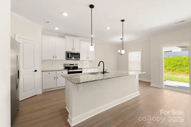 a kitchen with stainless steel appliances granite countertop a sink a microwave oven a refrigerator and white cabinets with wooden floor